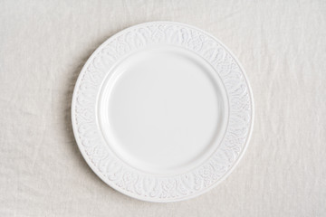 Top view of the white empty ceramic plate on linen tablecloth with copy space.  Concept food table serving.