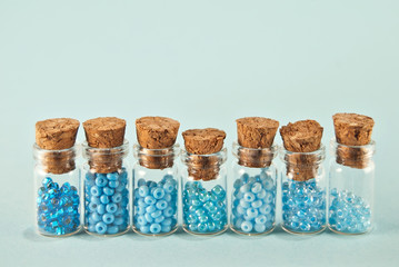 Purple and cyan beads in glass jars on bright blue background. Beads in a transparent container with a wooden cork. The concept of orderliness, balance and chaos.
