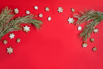 A Christmas homemade gingerbread cookies in the form of a snowflake sprinkled with icing sugar hanging around a pine branch with hoarfrost. Flat lay on red background with copy space.