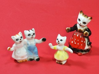 A set of four small cute porcelain cats that form a family: mother, two daughters and a son. The mother and daughters are dressed in colorful dress and the son is dressed in blue pants with suspender.