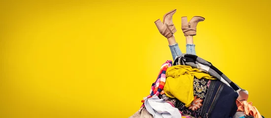 Fotobehang woman legs out of clothes pile on yellow background with copy space © ronstik