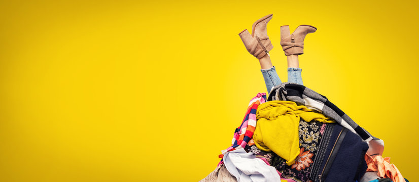 woman legs out of clothes pile on yellow background with copy space