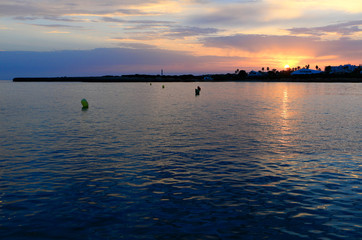 Sunset over the sea at Menorca (Spain) with buoys in the foreground and luxury houses in the background