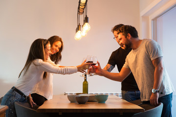 Joyful friends having fun and toasting wine at dining table. Young men and women in casual meeting indoors. Celebrating success concept