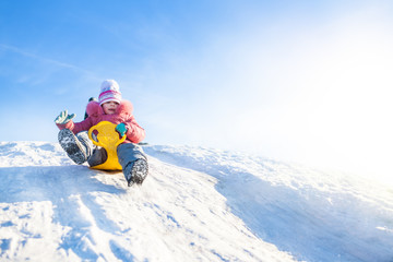 Happy small girl in winter clothing riding downhill