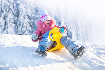 Fototapeta na wymiar Happy small girl in winter clothing riding downhill on snow with winter