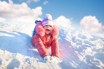 Fototapeta na wymiar Small girl in winter clothing riding downhill on snow with hands forward