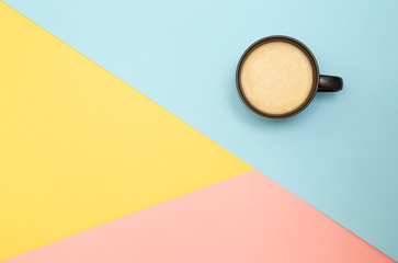 Flatlay coffee on a blue-yellow-pink triangles background. With copy space