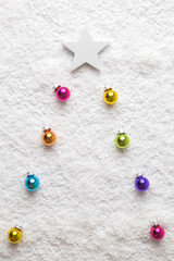 Christmas background abstract made of multicolored decoration baubles as fir tree and white star in snow.