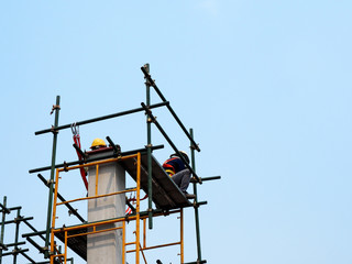Fototapeta premium Construction workers working on scaffolding with blue sky at construction site