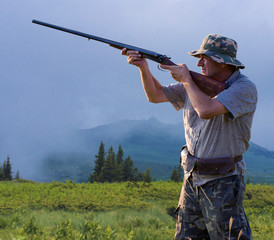 Fototapeta premium Hunting period, autumn season open. A hunter with a gun in his hands in hunting clothes in the autumn forest in search of a trophy. A man stands with weapons and hunting dogs tracking down the game...