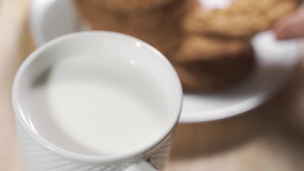 A woman hand dunks a cookie in the milk mug during the breakfast in a warm morning.