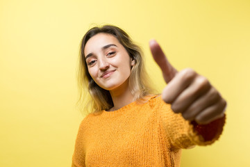 Happy young caucasian female in an orange sweater making thumb up sign and smiling. Good job and respect...