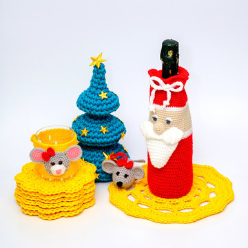 Home decor concept for new year and christmas. Photo of knitted decor thread for a bottle of champagne and a glass with a toy toy mouse, Christmas tree and yellow napkins on a white background.