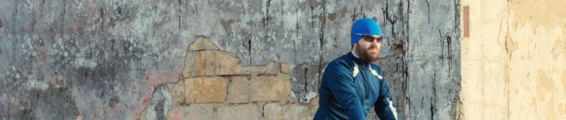 Athletic young guy with glasses looks into the distance. Toned panoramic image on a background of a brick wall with concrete.