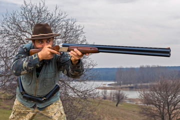 Fototapeta premium Hunting period, autumn season open. A hunter with a gun in his hands in hunting clothes in the autumn forest in search of a trophy. A man stands with weapons and hunting dogs tracking down the game...