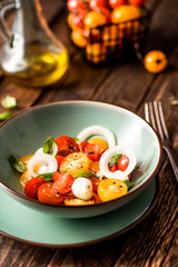 Yellow and red cherry tomatoes salad with fresh basil, mozzarella cheese and onion