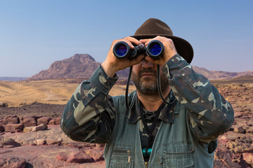 A hunter in a hat with binoculars looks out for prey	