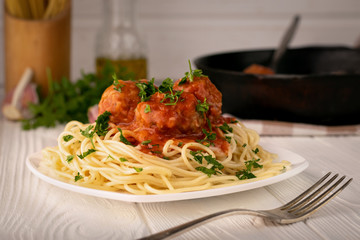 Plate of spaghetti with meatballs in tomato sauce on a wooden kitchen table