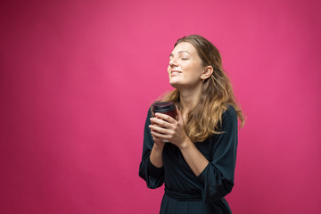 Glamor woman in glasses in a blue sweater with a drink of coffee on a pink background.	