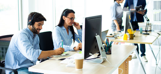 Attractive business people in headsets are smiling while working with computer in modern office
