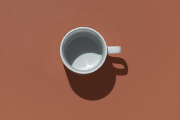 Empty tea cup on brown paper background. Coffee mug from above. Minimal concept Hard shadow. Flat lay, top view.