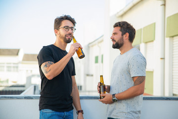 Two male friends enjoying party, chatting, drinking beer on outdoor terrace. Two young men in casual meeting outside. Beer party on terrace concept