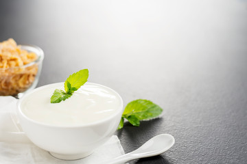Yogurt in a white cup with a healthy breakfast cereal placed on the black table.