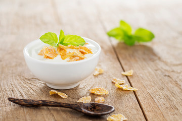 Yogurt in a white cup with a healthy breakfast cereal, placed on a wooden table