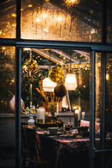 Decorated greenhouse in trendy christmas setting with dinner table, candles and christmas lights.