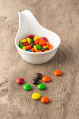 Colorful candies on a white spoon and spread over wooden table.