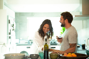 Cheerful couple drinking wine, laughing and having fun in kitchen. Young man and woman in casual meeting indoors. Happy couple concept