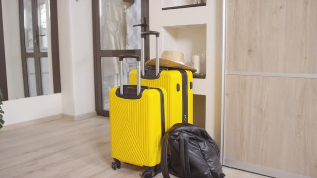 Dolly-in shot of black backpack and yellow suitcases standing in hallway of house