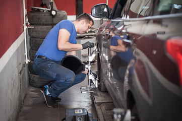 Wheel alignment. Car mechanic installing sensor during suspension adjustment