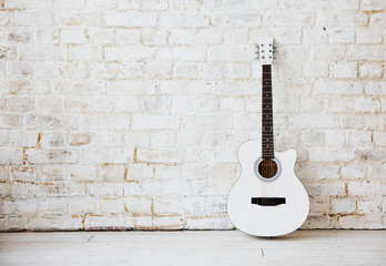 Fototapeta na wymiar Acoustic white guitar leaning against a white wall in an empty room