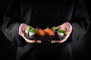 Fotobehang Sushi served on stone slate in chef hands on dark background. Decorated sashimi nigiri with salmon and avocado. Traditional japanese food. Copy space for text © CrunchyBeans