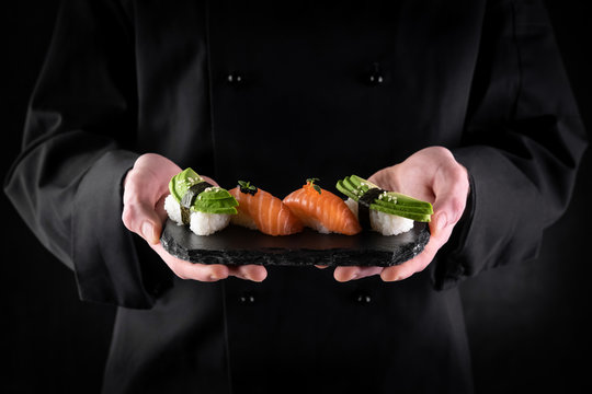 Sushi served on stone slate in chef hands on dark background. Decorated sashimi nigiri with salmon and avocado. Traditional japanese food. Copy space for text