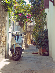 a scooter parked in a narrow typical quiet cobbled street in rhodes town with old yellow painted...
