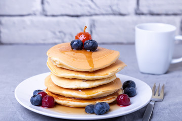 Pancakes with maple syrup, blueberries, cherries and a mini apple. A cup of coffee in the background. Traditional american pancakes. Close-up.