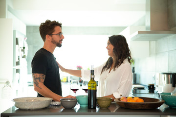 Cheerful trendy couple chatting over glass of wine in kitchen. Young man and woman in casual meeting indoors. Happy couple at home concept
