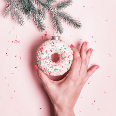 Female hand hangs Christmas bauble made of glazed donut on pink background. Christmas creative...