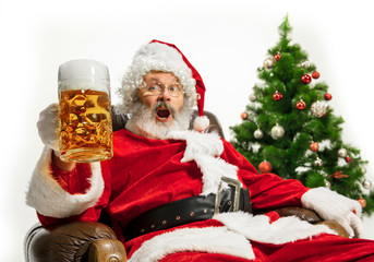 Santa Claus drinking beer near the Christmas tree, congratulating, looks drunk and happy. Caucasian male model in traditional costume. New Year 2020, gifts, holidays, winter mood. Copyspace for your