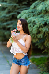 Smiling young woman holding mojito while walking in the summer street