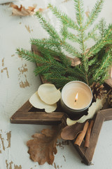 Soy candle with a Christmas tree branch, cones and leaves in a star-tray. Christmas composition for home decor.