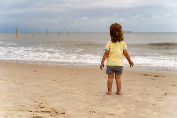 kleines Kind allein am Strand bei wolkigem Wetter