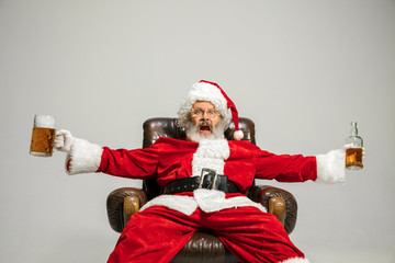 Santa Claus drinking beer sitting on armchair, congratulating, looks drunk and happy. Caucasian...