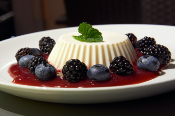 Delicious panna cotta with blackberries and blueberries. Decorated with mint. Served on the white...