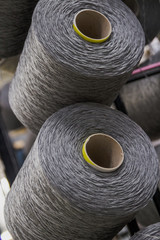 Large collection of thread and yarn in rolls stacked high on a metal grid ready to be fed down to a machine to weave them all together an industrial commercial factory create textiles materials rugs