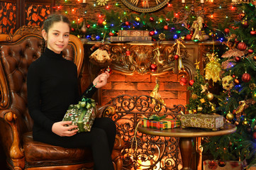 Portrait of cute happy girl sitting with gift by Christmas tree