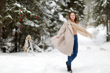 Fototapeta na wymiar happy young woman in winter day outdoors in forest. background of tree branches in the snow and decorated with Christmas decorations.
